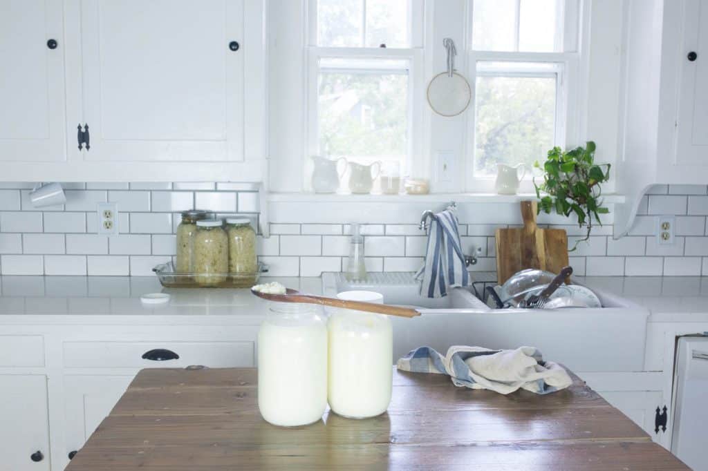 two half gallon mason jars full of milk kefir with a wooden spoon on top. Mason jars are on a wood counter top.