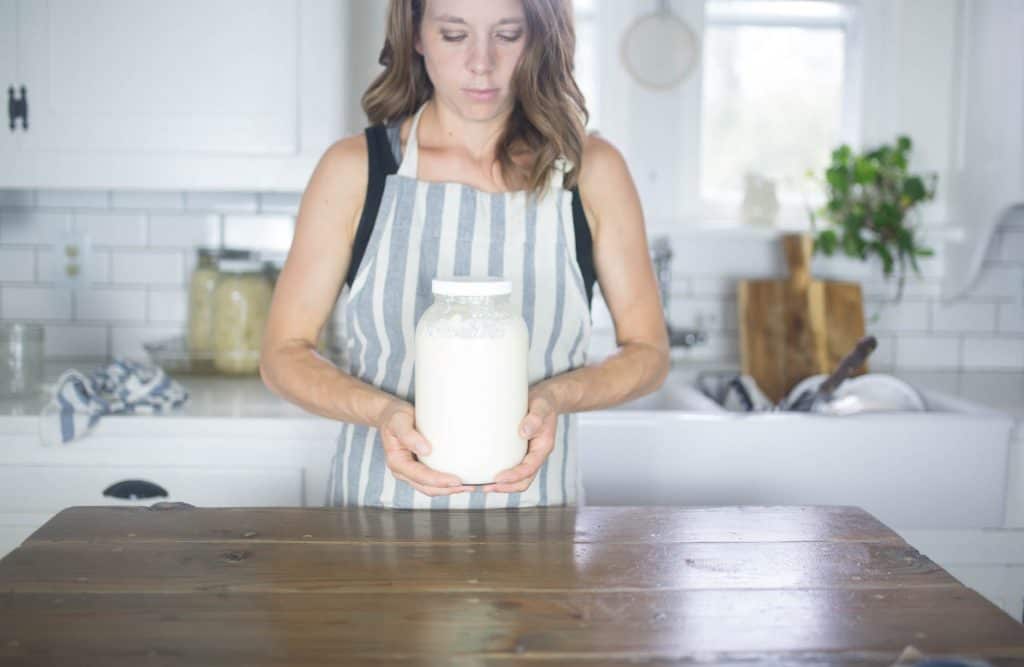 women wearing a blue and white striped apron holding mason jar of milk kefir 