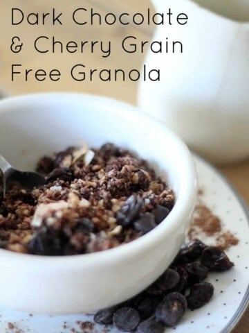 a white bowl filled with grain-free granola with chocolate chips and cherries on a silver and white polka dot plate