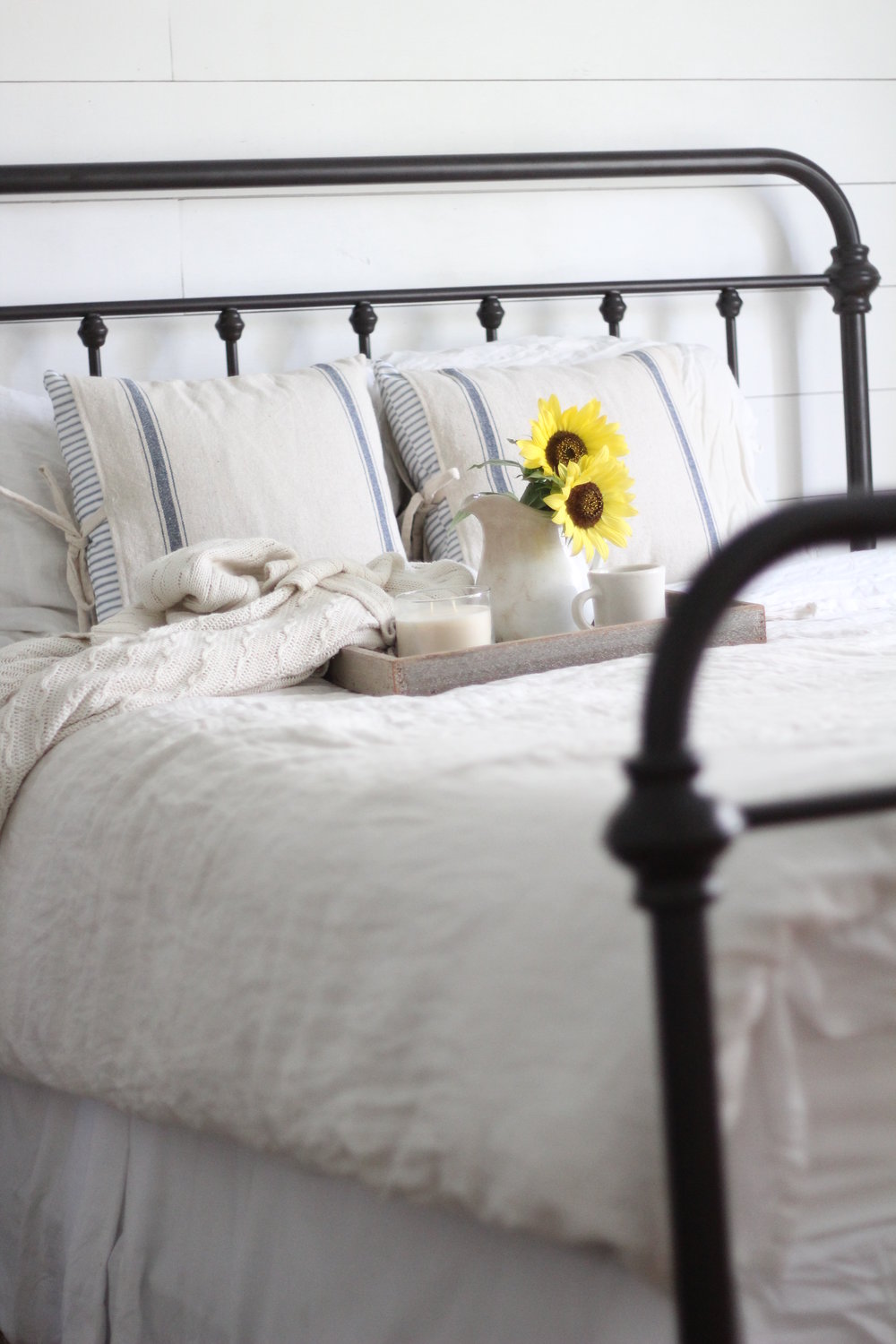 iron bed with linen bedding and a serving tray with a vase of flowers