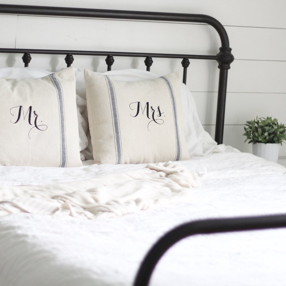 iron bed with linen bedding. a faux ikea plant in a white pot to the right