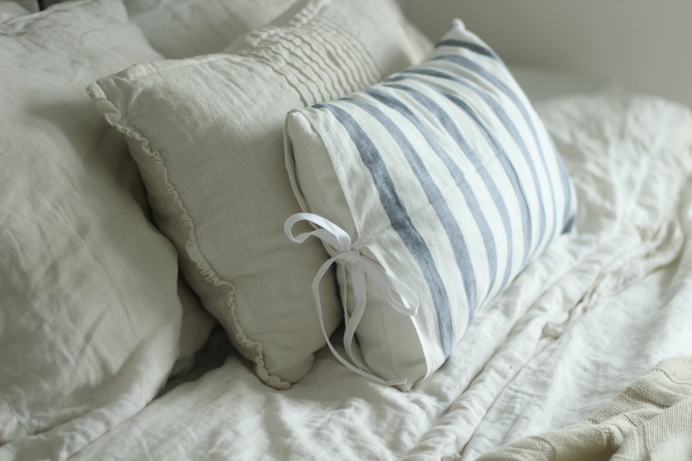 linen duvet and pillows on a bed. A blue and white stripped ikea towel pillow in front