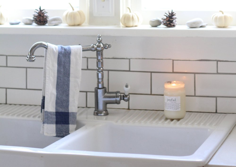 ikea farmhouse sink with a antique inspired faucet and a ikea tea towel hanging off the faucet. A candle is to the right.