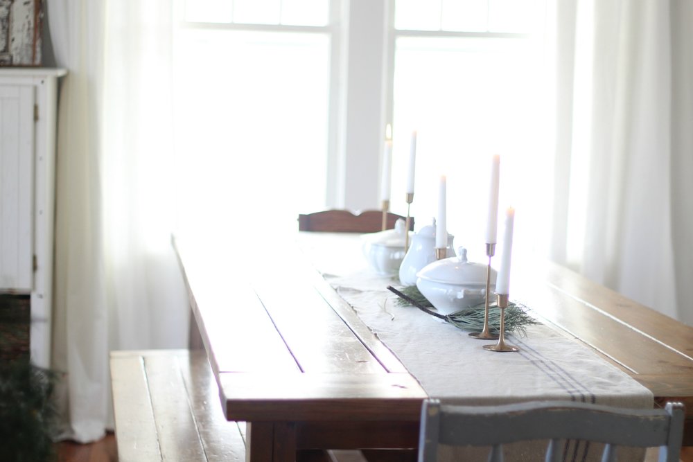 wooden table with a grain sack table runner, white serving canisters and gold candle stick holders