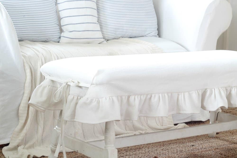 white drop cloth DIY bench slipcover on a white bench with a white couch with pillows in the background