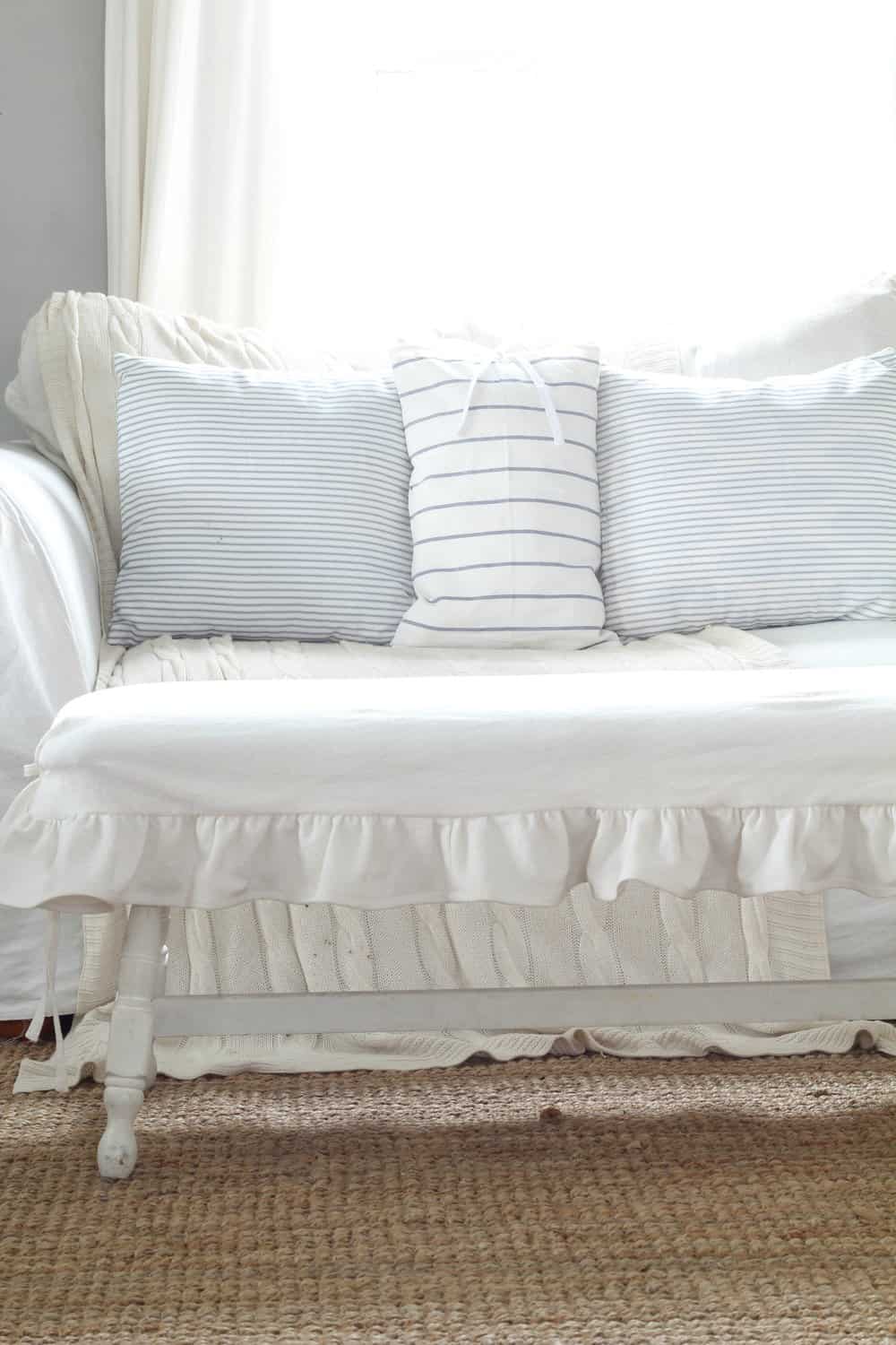 white bench with ruffle slipcover with a white couch with blue pillows in the background