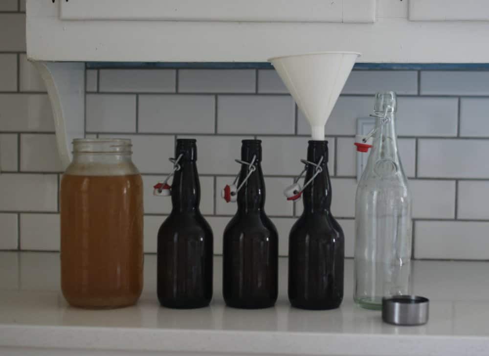 half gallon mason jar filled with water kefir with four empty bottles ready for bottling to the right