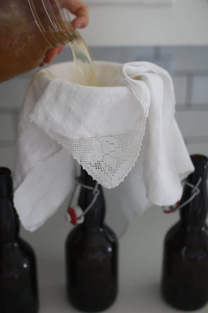 straining water kefir into a glass bottle with a funnel lined with cloth