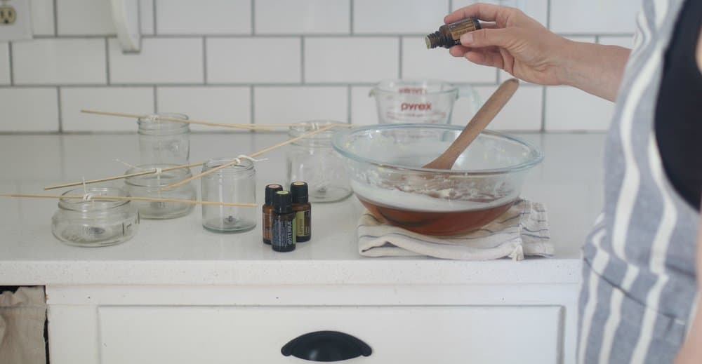 adding essential oils to glass bowl full of coconut oil and beeswax