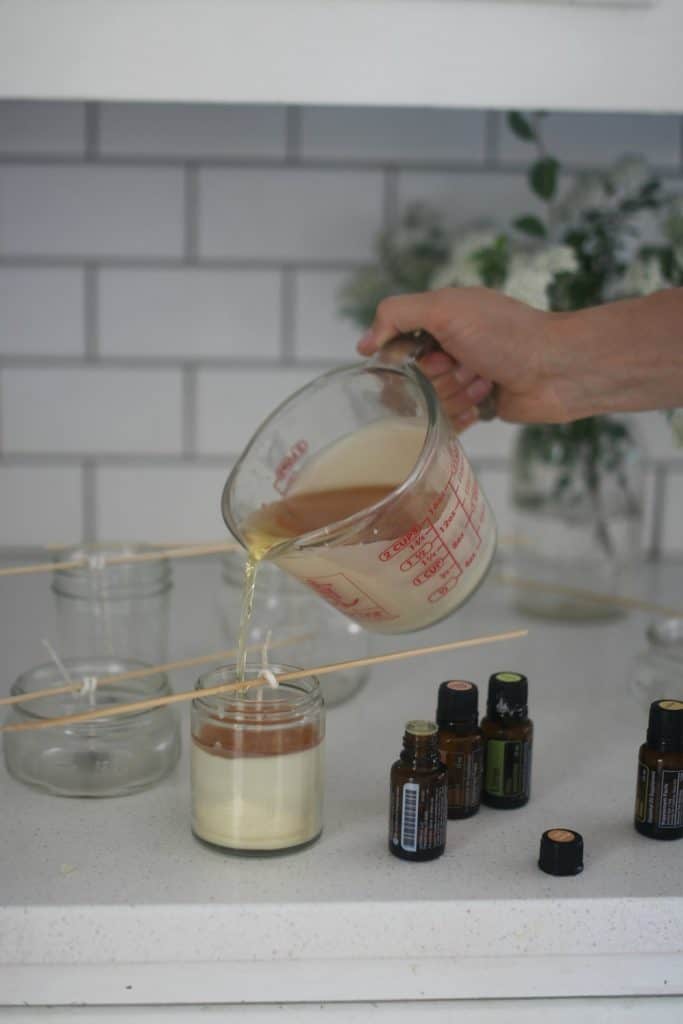 pouring melted beeswax, coconut oil mixture into mason jars with wicks