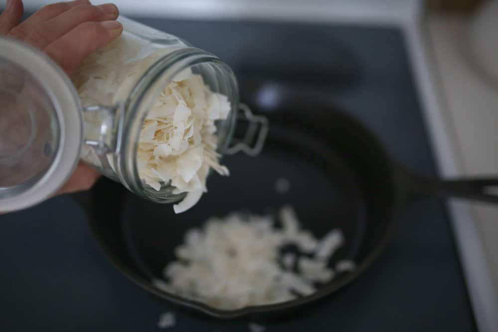 coconut flakes being poured into a cast iron skillet.