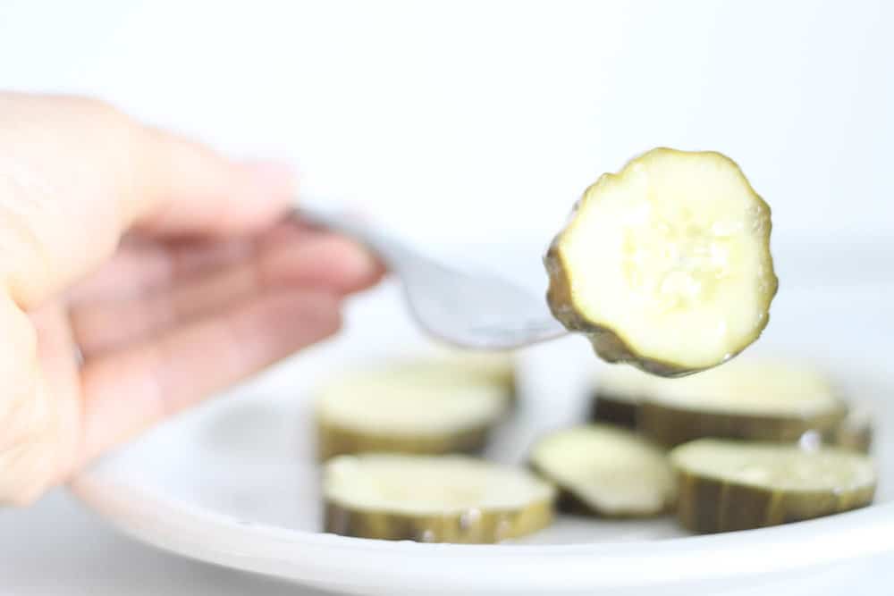 fermented pickle on a fork with more pickles on a white plate