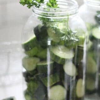 cucumber slices and parsley in a half gallon mason jar on a white countertop with a white backsplash in the background
