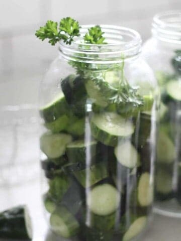 cucumber slices and parsley in a half gallon mason jar on a white countertop with a white backsplash in the background