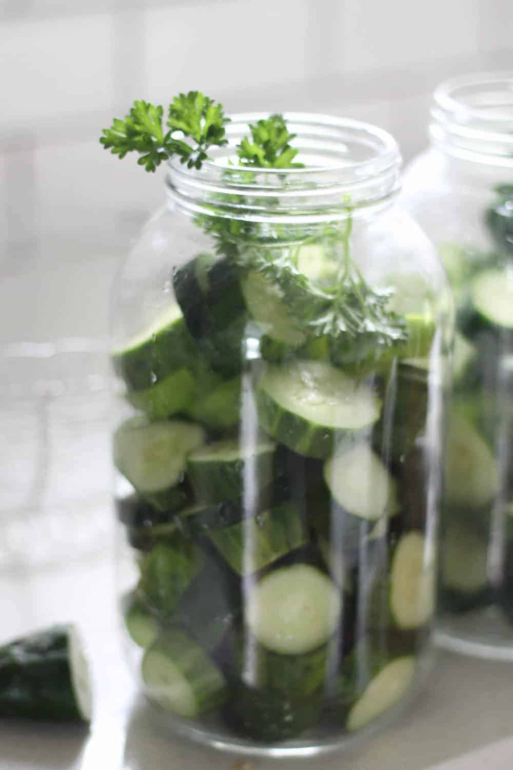 cucumber slices and parsley in a half gallon mason jar on a white countertop with a white backsplash in the background