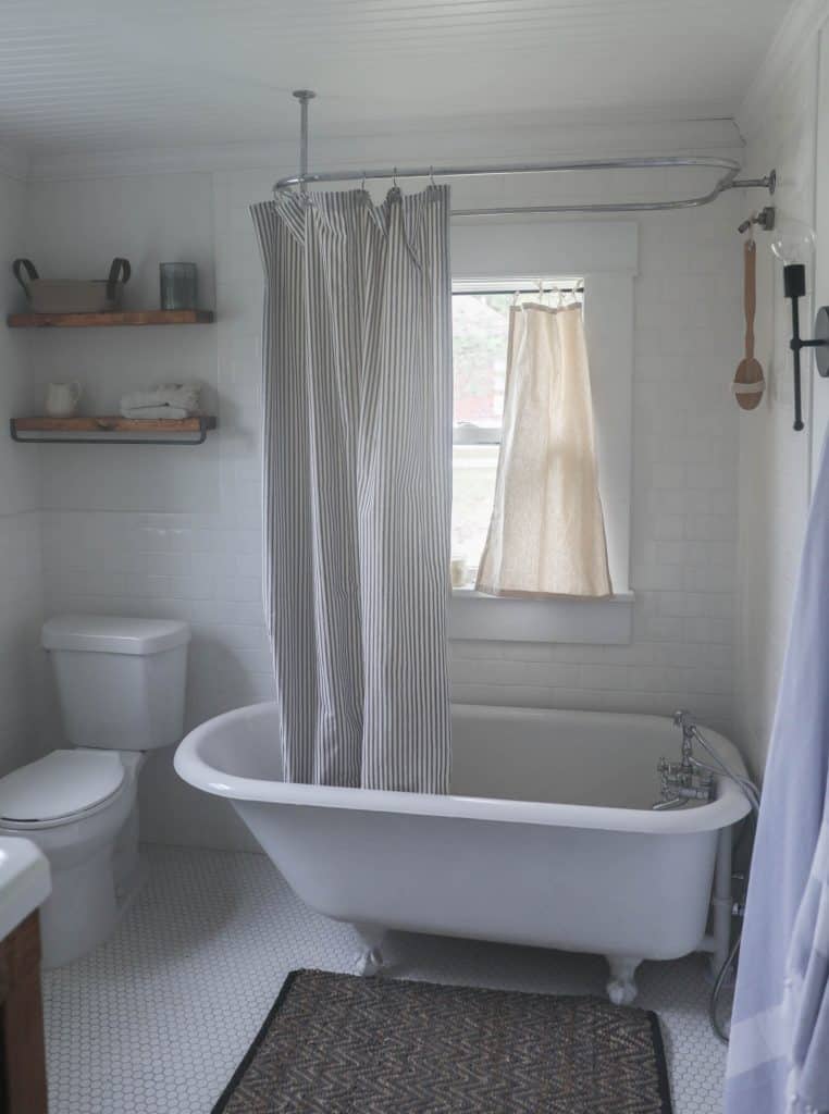 drop cloth curtains hanging in a window over a bathtub in a farmhouse bathroom with a claw foot tub