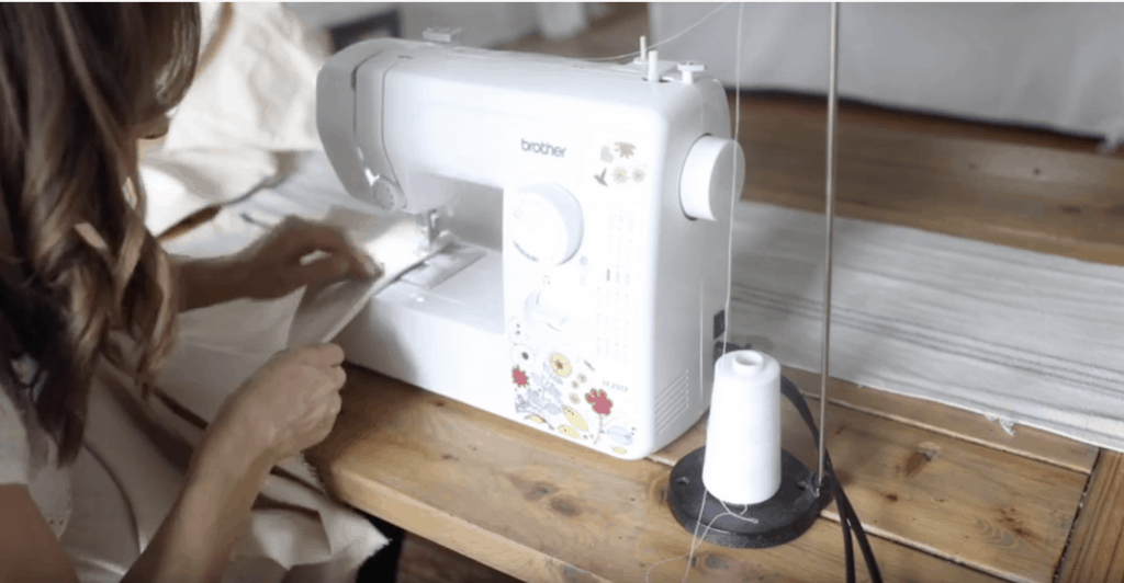 women hemming drop cloth on a white sewing machine with flowers to make drop cloth curtains