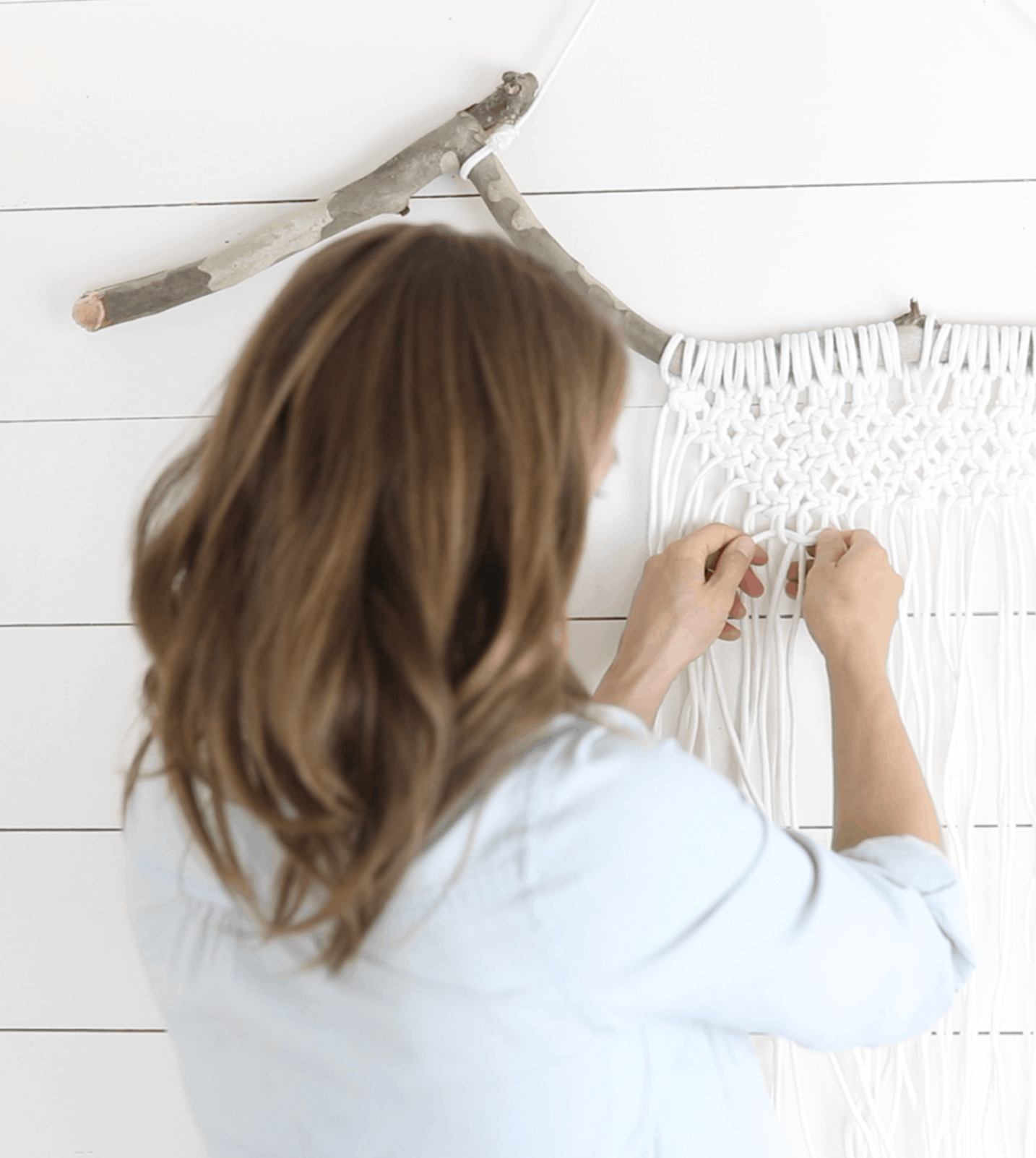 woman tying macrame on a wood branch for a diy macrame wall hanging