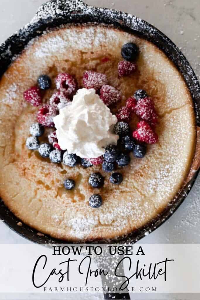 sourdough dutch baby in a cast iron skillet topped with frozen raspberries and blueberries with whipped cream and powdered sugar on top