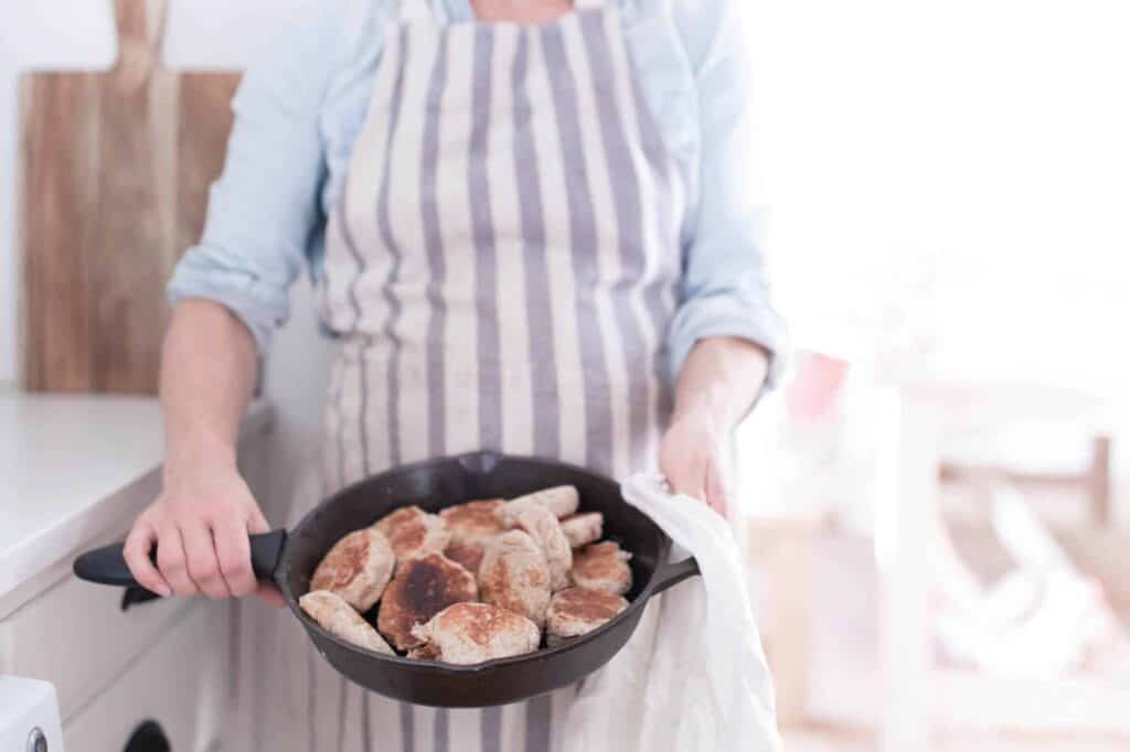 women holding a cast iron skillet full of sourdough English muffins