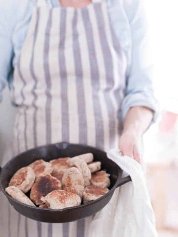 women holding a cast iron skillet full of sourdough English muffins