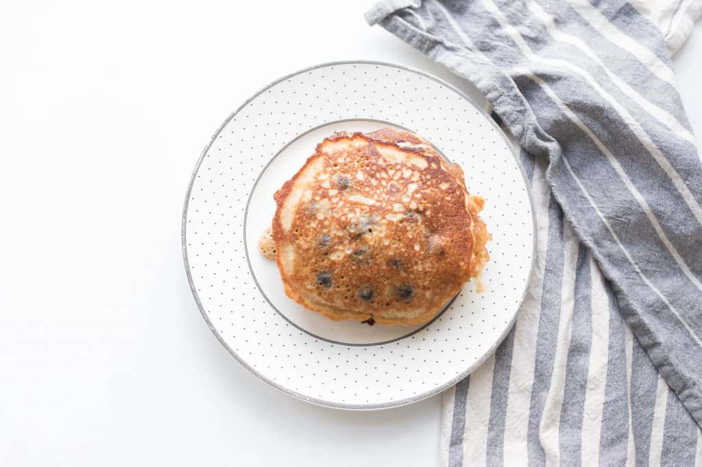 Blueberry Sourdough Pancakes on a white plate with gray polka dots next to a white and blue towel