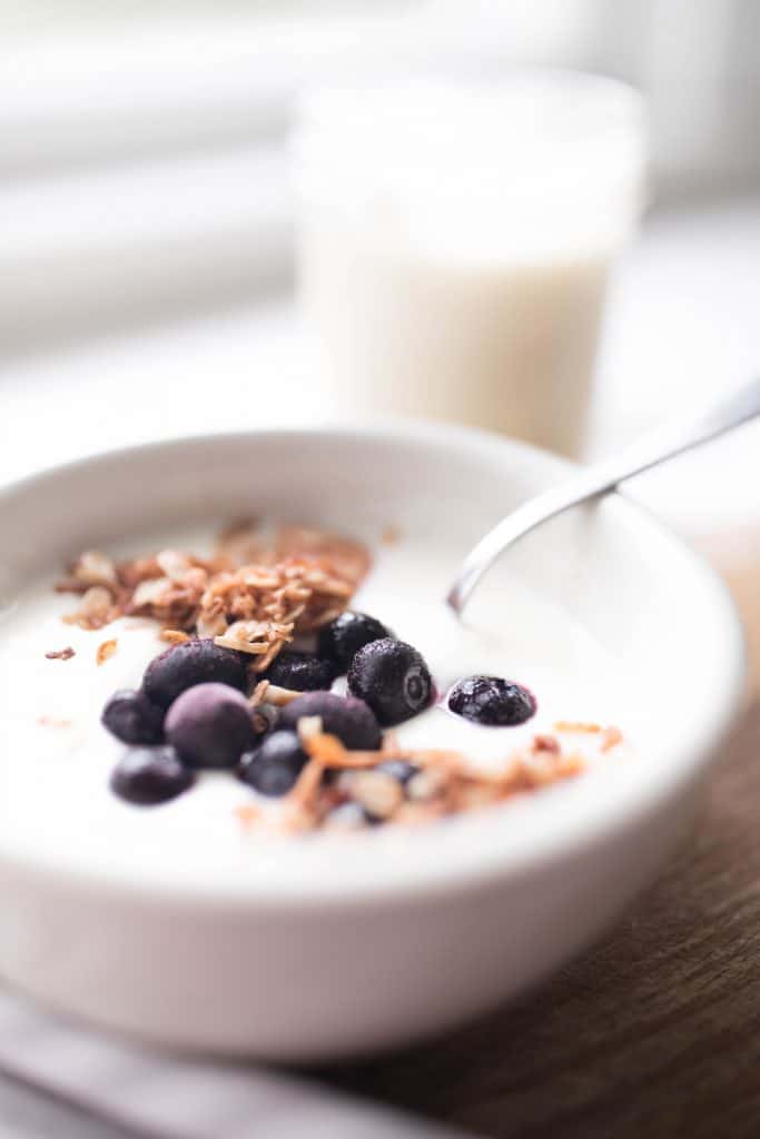 a white bowl of yogurt topped with frozen blueberries and granola