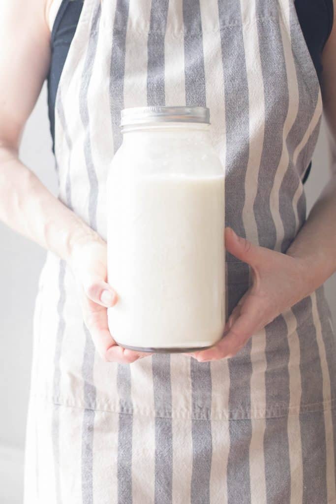 A women wearing a stripped apron holding a half gallon of yogurt.