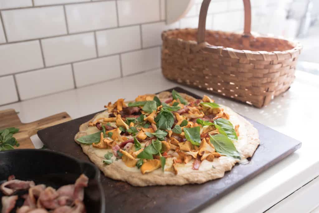 bacon chanterelle sourdough pizza topped with fresh herbs on a pizza stone ready for the oven