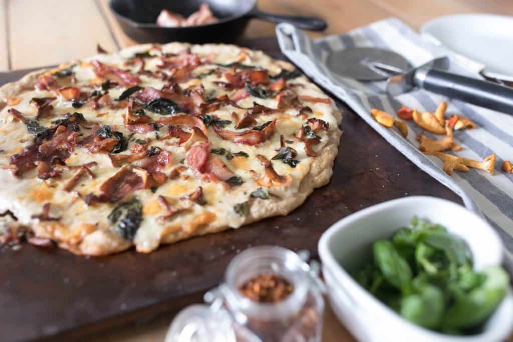 sourdough pizza with chanterelle mushrooms and cheese on a wood cutting board with ingredients spread around