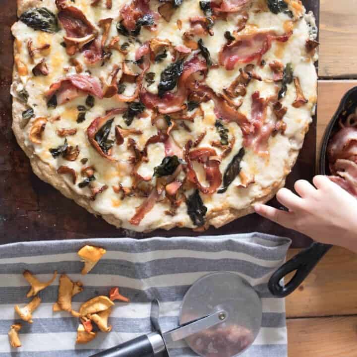 overhead shot of bacon chanterelle mushroom pizza on a pizza stone with ingredients surrounding itforaging chantrelle mushrooms wild edibles