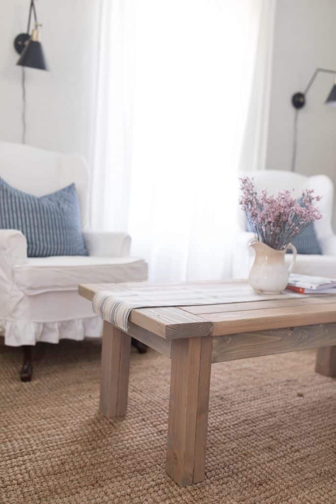 farmhouse coffee table with two white chairs with blue pillows behind it