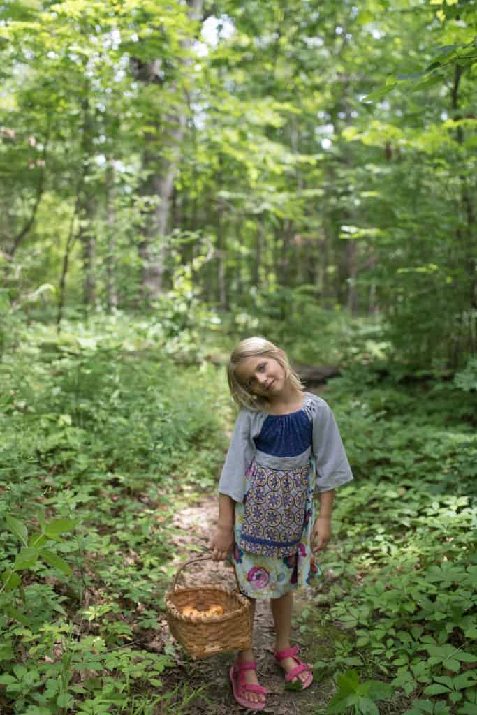 little girl in the woods holding a basket of wild chanterelle mushrooms from foraging