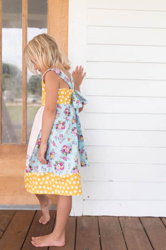 girl wearing a handmade dress with florals, polkadots, and bows on her front porch