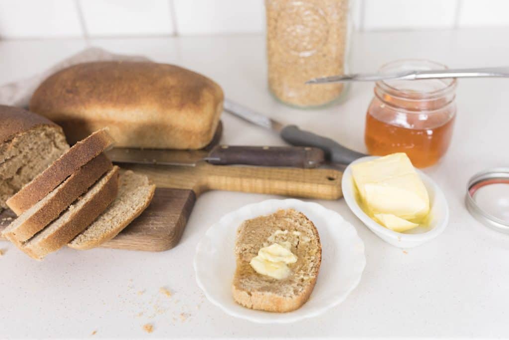whole wheat sourdough bread recipe sliced on a cutting board. One slice of bread on a white plate with butter.
