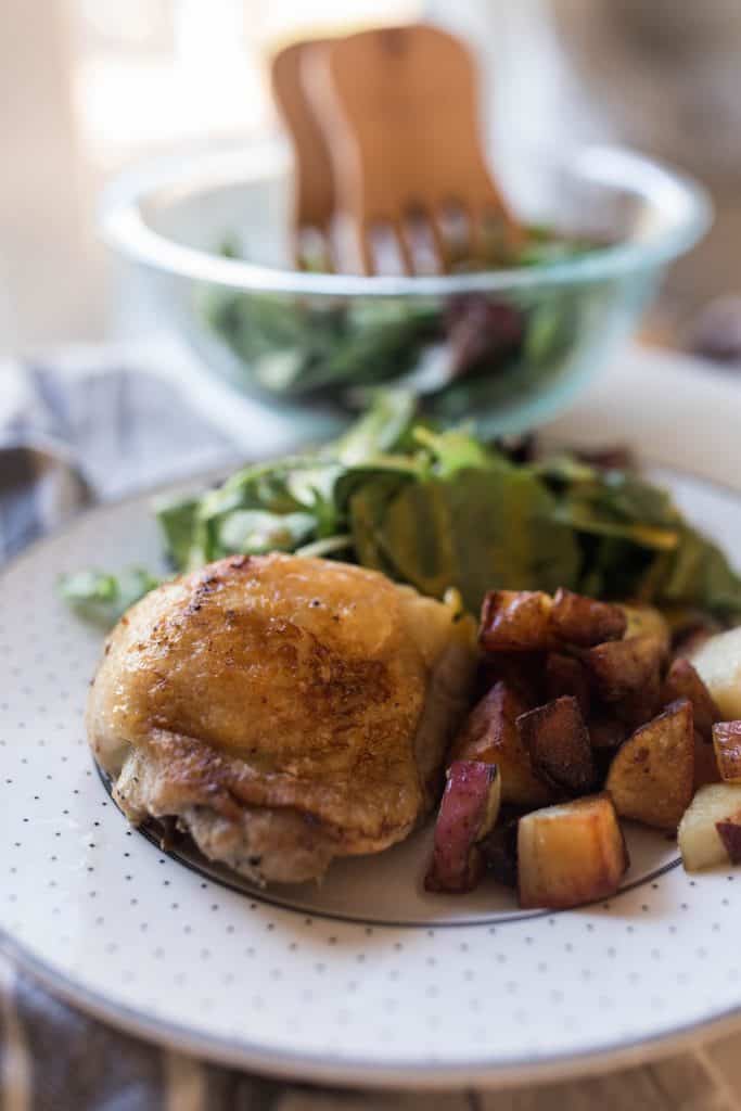 crispy chicken on a plate with potatoes to the right and a fresh green salad behind