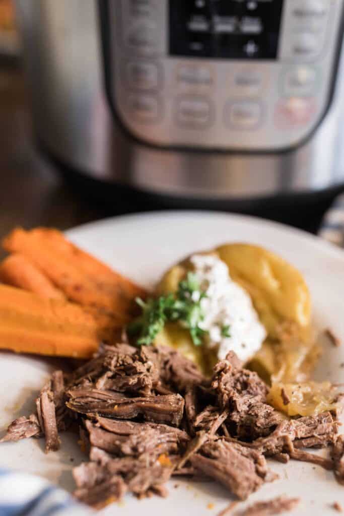 tender pot roast shredded on a white plate with carrots and potatoes.