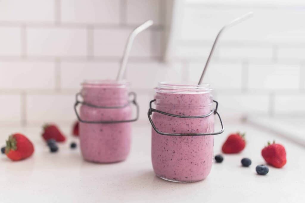 two jars of berry kefir smoothie with metal straws and berries spread out on the counter