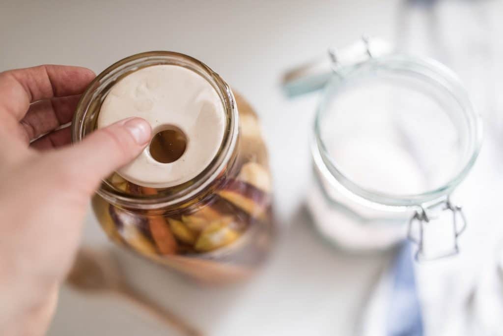 hand placing a fermentation weight on top of carrots in a salt water bring to make fermented carrots