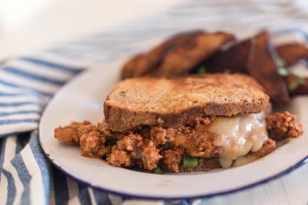 turkey sloppy joes with melted cheese on homemade sourdough bread on a vintage white plate on a blue and white stripped napkin