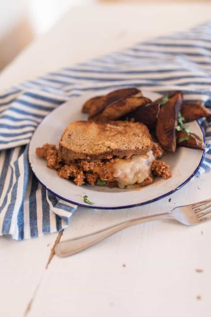 homemade turkey sloppy joes with melted cheese on thick sliced bead with potato wedges on a white vintage plate. The plate sits on a white and blue stripped napkin with a fork in front