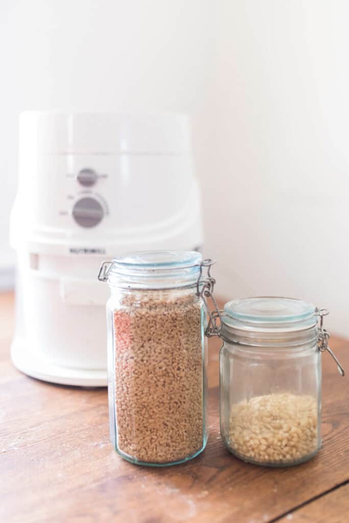 two jars of wheat berries on a wood countertop with a Nutrimill in the background