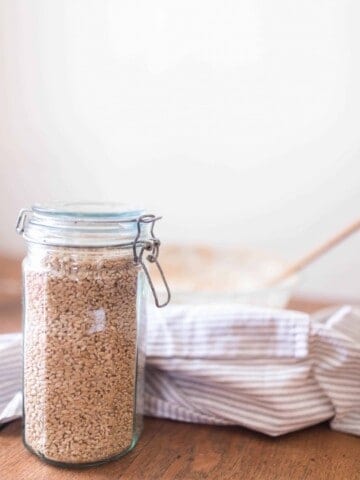 jar with a swing top lid full of wheat berries on a wood table with a bowl and linen stripped towel in the background