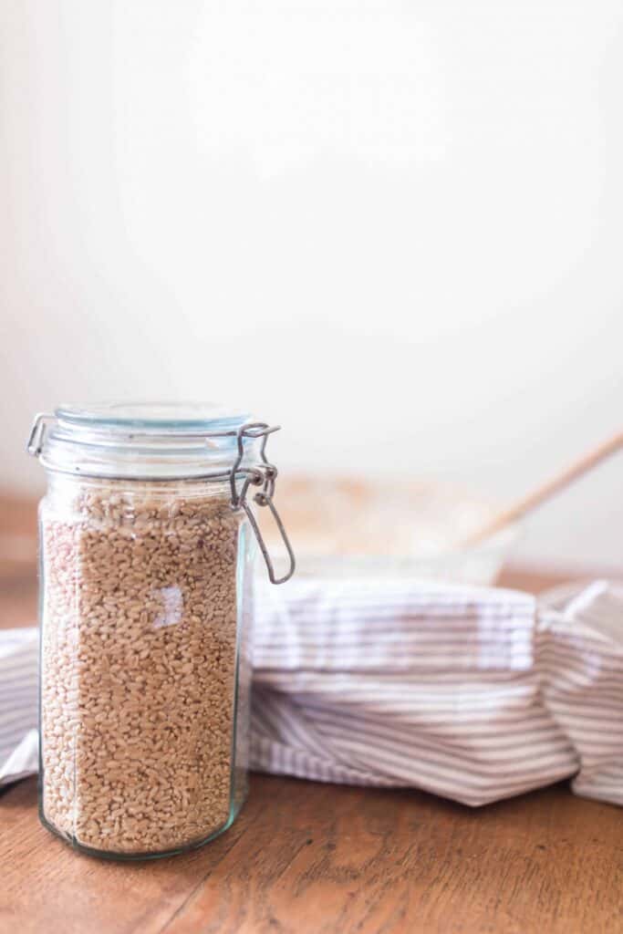 jar with a swing top lid full of wheat berries on a wood table with a bowl and linen stripped towel in the background