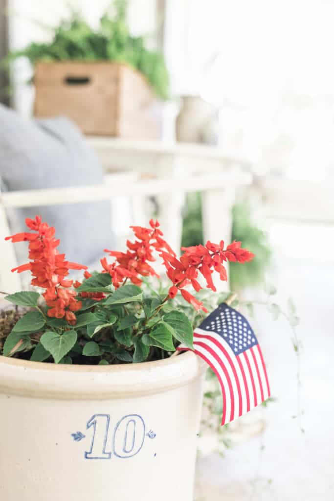 scarlet sage salvia in a crock with an american flag with a rocking chair behind it