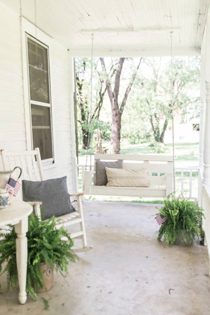 porch swing with farmhouse pillows, a rocking chair to the left with a blue pillow