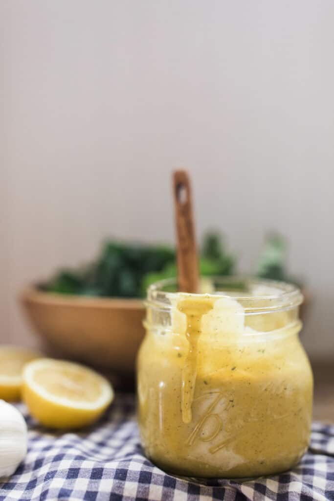 honey mustard dressing in a glass jar with a wooden spoon in the jar and a salad behind it