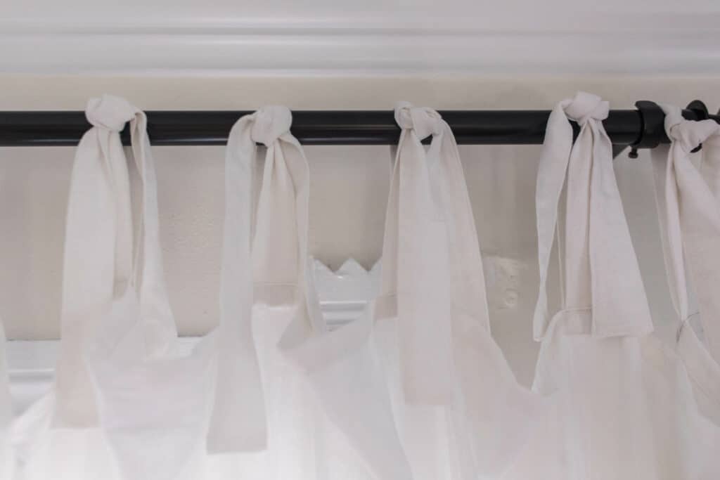 close up of white tie-top curtains on a black curtain rod