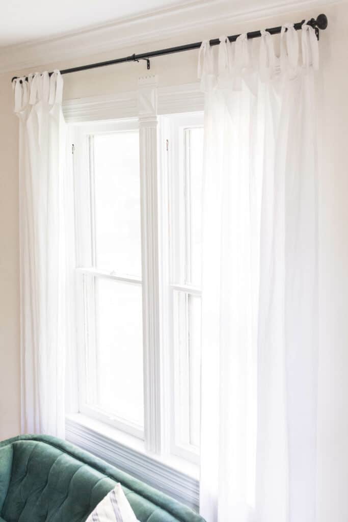 white tie top curtains on a black curtain rod next to a green velvet love seat