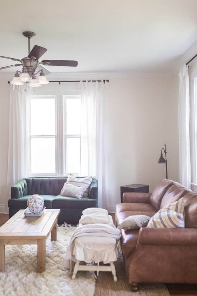 white tie top curtains in a living room with a leather couch, green loveseat and coffee table